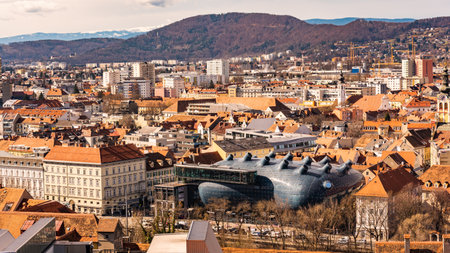Graz, Austria - 10.03.2020: The top of the Kunsthaus art museum in Graz Austria stands in contrast to the surrounding terra cotta roof topsのeditorial素材