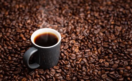 Hot steaming Espresso Cup of coffee on table covered with coffee beans. Copy space background
