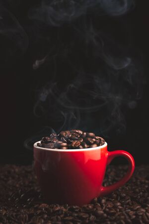 Red Cup with smoking and steaming coffee beans on table covered with coffee beans.Coffe themed backgroundの写真素材