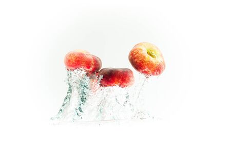Bunch of doughnut peaches isolated on white, splashing into water. Fruits sinking in crystal clear water with air bubblesの写真素材