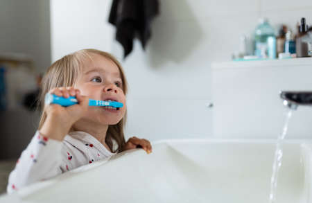 Baby girl in bright bathroom brushing her teeth above the sink. 2-3 years old child personal hygiene.の写真素材