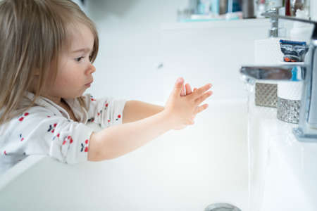 Cute little girl 2-3 years old washing hands with soap and water in bright bathroom. Adorable child...