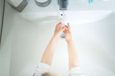Cute little girl 2-3 years old washing hands with soap and water in bright bathroom. Adorable child learning cleaning body parts. Morning hygiene routine. Happy healthy kid at home or nursery. Top Viewの写真素材