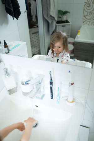 Cute little girl 2-3 years old washing hands with soap and water in bright bathroom. Adorable child learning cleaning body parts. Morning hygiene routine. Happy healthy kid at home or nursery. Mirror reflectionの写真素材