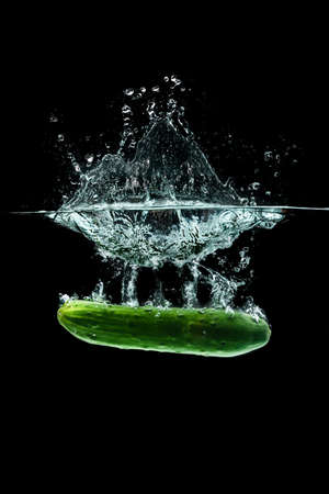 Cucumber splashing water isolated onblack background. Healthy food conceptの写真素材