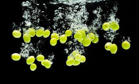 White grape berries splashing into water against black backdrop. Splash photography.の写真素材