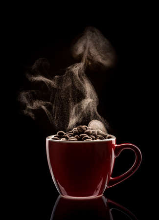 Steaming red cup filled with coffee beans against black backgroundの写真素材