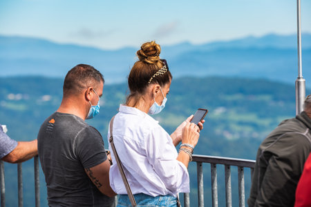 Lake Worth, Austria - 26.08.2020: People with masks on the top of The Pyramidenkogel wooden observation tower with view over lake. Corona virus pandemic timeのeditorial素材
