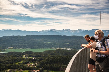 Lake Worth, Austria - 26.08.2020: People with masks on the top of The Pyramidenkogel wooden observation tower with view over lake. Corona virus pandemic timeのeditorial素材