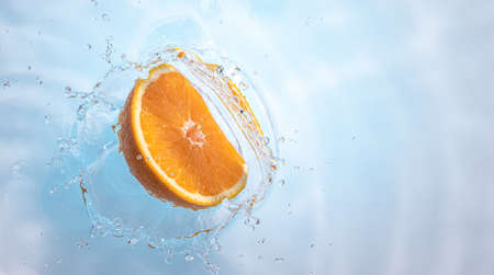 Fresh ripe half of orange splashing into clear water, isolated on light blue background. Health food...