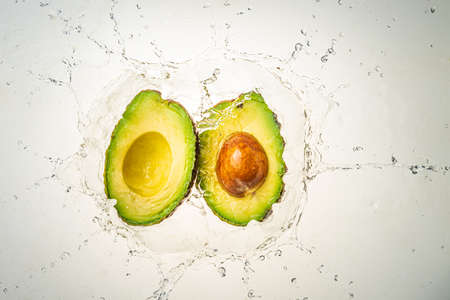 Two halves of avocado splashing into clear water, isolated on light blue background. Health food conceptの写真素材