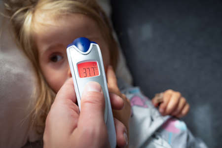 Parent takes temperature for her child with infrared thermometer at home, low-grade feverの写真素材