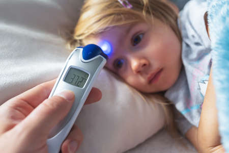 Parent takes temperature for her child with infrared thermometer at home, low-grade feverの写真素材