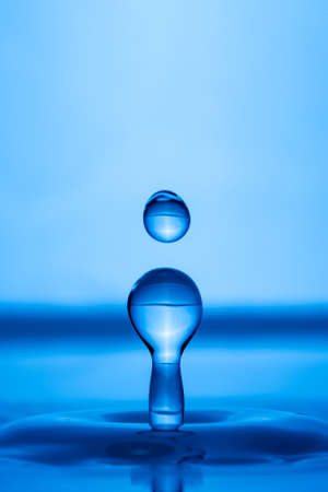 Water drop splashing into blue water surface. Health and purity conceptの写真素材