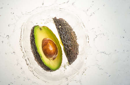 Two halves of avocado splashing into water, isolated on white background. Copy space. Health food...