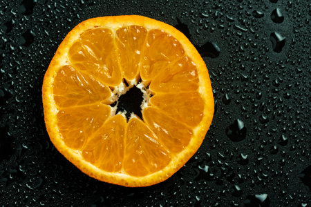 Mandarin slice, detailed closup against black background coverd with water drops.の写真素材
