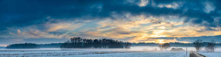 Landscape panorama with road, white fields cover by snow and sunset sky.の写真素材