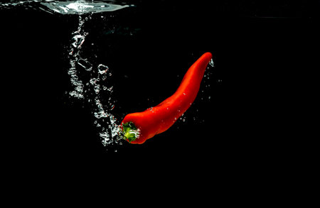 Red pepper falls to the water, causing bubbles and scattered water.の写真素材