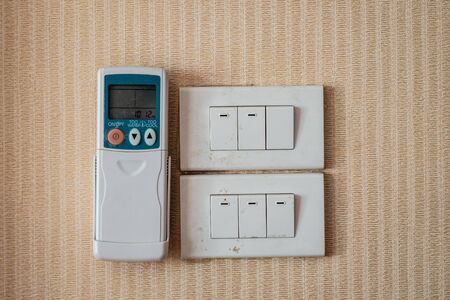 An air-conditioner remote with hanger and six light switches on brown stripe background