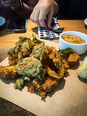 Signature homemade crispy fried calamari with lemon slices and dipping sauces on a wooden trayの写真素材