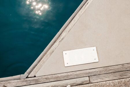 An aluminum signboard with copy space, mounted on the concrete floor with nearby wooden floor and sun flares on the sea waterの写真素材