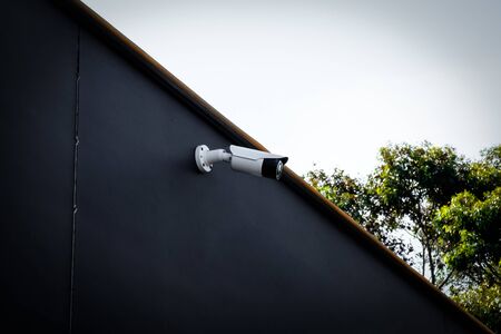 Modern white outdoor security/cctv camera installed on a black painted wall at the chocolate store...