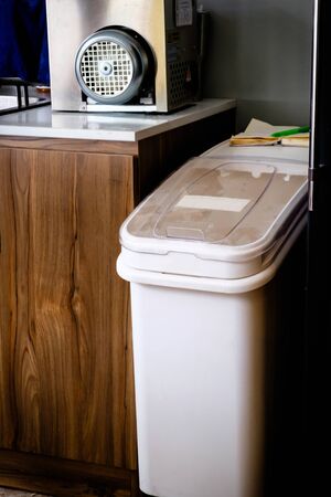 A white plastic garbage bin with clear cover standing beside wooden cabinet inside the restaurantの写真素材