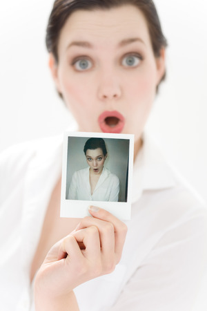 Young woman holding her own polaroid and making faces. Focus on polaroid.の写真素材