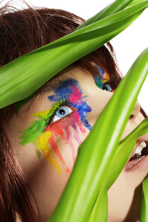 Fashion model with short dark fluffy hair and colorful make-up posing with a green plant.の写真素材