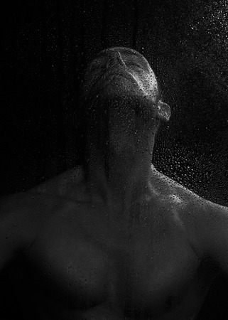 Bare man with expressive pose behind wet glass.の写真素材