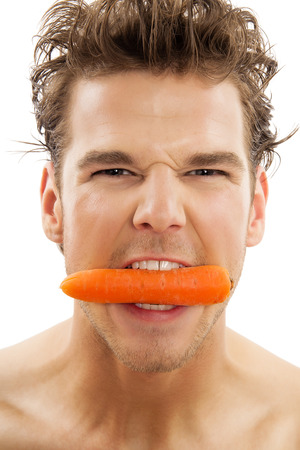 Young active Caucasian man vigorously biting a peeled carrot over white background. Healthy eating habits concept.の写真素材