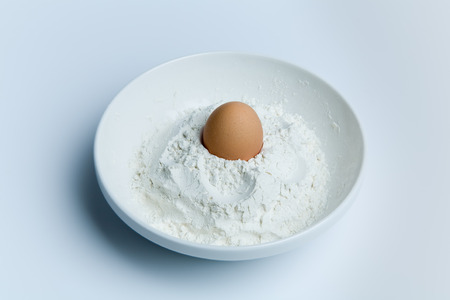 Whole fresh chicken egg and flour in a bowl over blue.