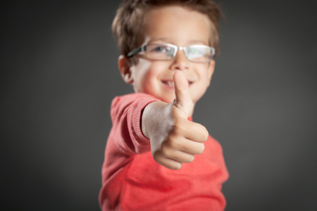 Little happy boy with thumb up approval gesture. Studio shot portrait over gray background. Fashionable little boy.の写真素材