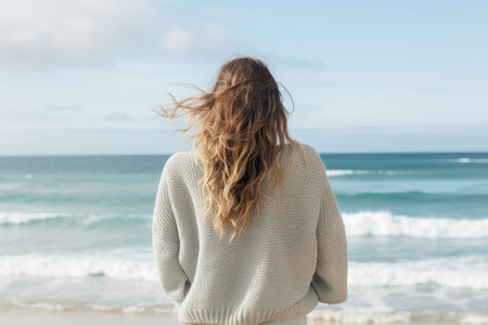 Freedom of the coast as a young woman stands by the water's edge, her long hair and carefree expression capturing the essence of a carefree summer day.の素材