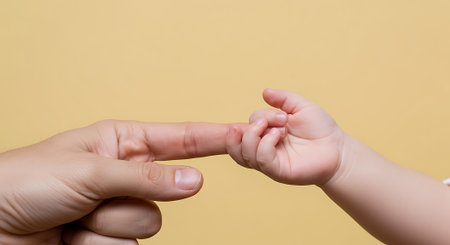 Close up of mother and child hands holding each other on yellow backgroundの素材
