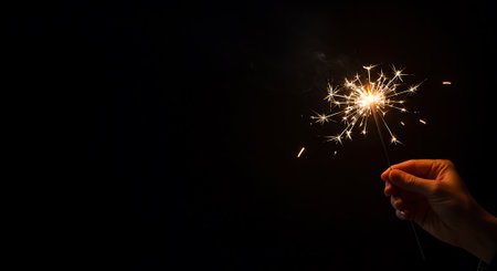 Burning sparkler in female hand on black background with space for textの素材