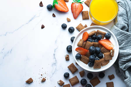 Cereal bowl with milk, blueberries and strawberries accompanied by tropical juice and ingredients with copy space. Gastronomic conceptの写真素材