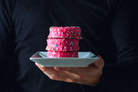 Man in black holding a white plate with a tower of strawberry donuts. Unhealthy cookingの写真素材
