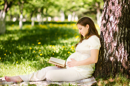 Beautiful pregnant woman in the park with bookの写真素材