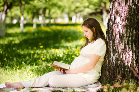 Beautiful pregnant woman in the park with bookの写真素材