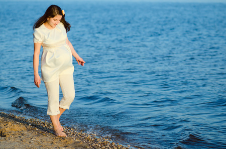 Beautiful pregnant woman walks along the shoreの写真素材
