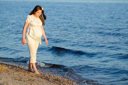 Beautiful pregnant woman walks along the shoreの写真素材