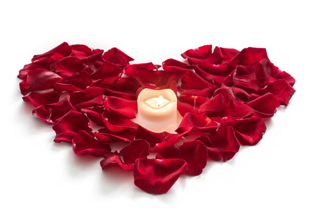 Rose petals in heart form with candle on white backgroundの写真素材