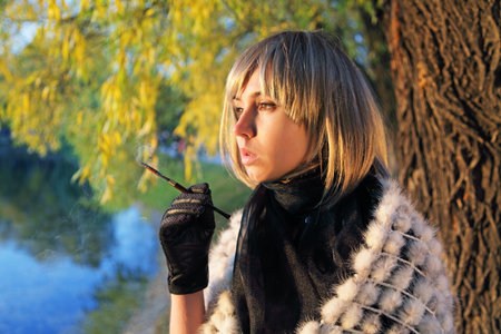 The thoughtful girl in a wig smokes a cigarette about a pond during a sunset