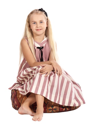 The girl in a striped dress sits on a padded stool, is isolated on a white backgroundの写真素材