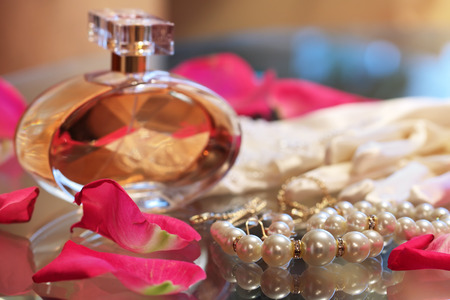 A bottle of perfume, a pearl necklace, and rose petals on the glass tableの写真素材
