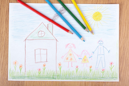 Some pencils lie in children's drawing with the image of a happy familyの写真素材