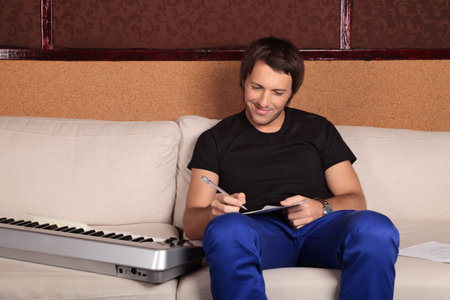 Musician composes a song sitting on the sofa with a synthesizerの写真素材