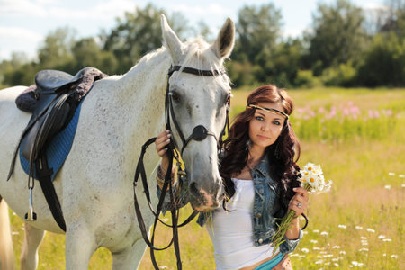 Beautiful girl walks on white horse on a summer meadowの写真素材