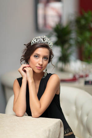 Beautiful girl in evening dress with a tiara on her head sits in a chairの写真素材